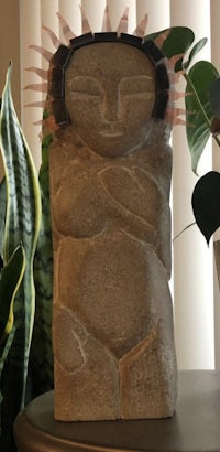 a statue of a woman sitting on a table next to a plant